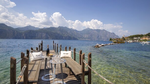 A wooden pier with a table set for two, clear water, mountains in the background, and a small town across the water. - Villa Locchi with private Pier (Malcesine)