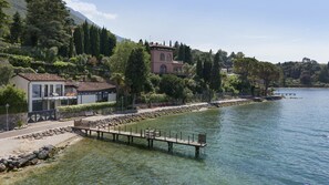 A lakeside property with a dock, a building with a balcony, and a mountain backdrop.
