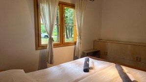Ein Schlafzimmer mit einem Bett, einem Fenster mit Vorhängen, einem Holzschrank und einem Handtuch auf dem Bett.
