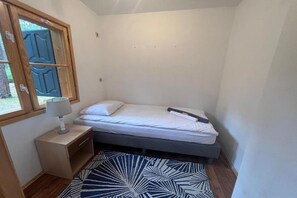 A small, single-bed room with a wooden nightstand, a lamp, and a patterned rug. - Holiday home with private garden, close to the sea (Pobierowo)