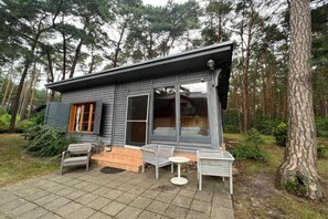 Uma cabana com varanda, área de estar externa e vista para a floresta ao redor.