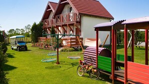 Una casa amb teulada vermella, un balcó de fusta i un parc infantil.