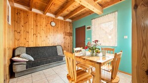 Una habitació acollidora amb sostre de fusta, un sofà, una taula de dinar amb cadire i una finestra amb cortina.