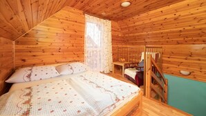 Un dormitori de cabana de fusta amb un llit, una finestra amb cortines, una escala de fusta i vistes a l'exterior.
