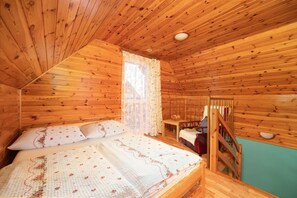 A wooden cabin bedroom with a bed, a window with curtains, a wooden staircase, and a view of the outside. - Two-story holiday homes with terraces, playground (Mielno)