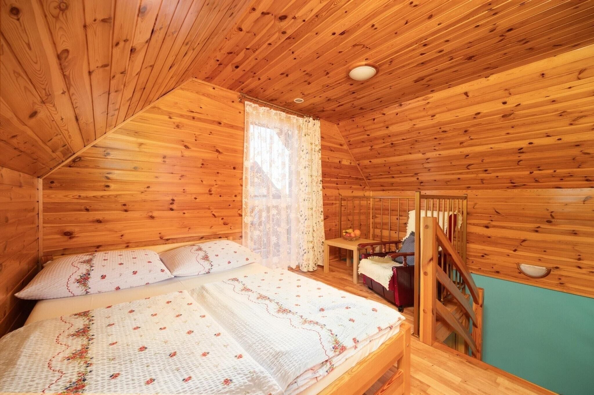 Ein Schlafzimmer in einer Holzhütte mit einem Bett, einem Fenster mit Vorhängen, einer Holztreppe und Blick ins Freie.