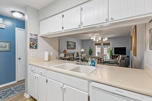 A kitchen with white cabinets, a double sink, and a dishwasher. - Brockinton Point Condo | Pool | Pets Allowed | Mid-Island Location | Full Kitchen | Patio | Deck (St. Simons Island)