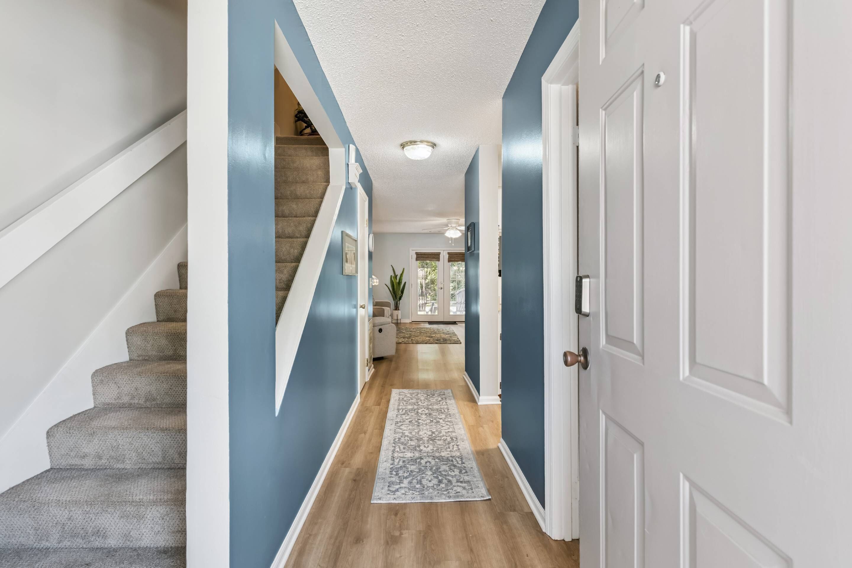 A hallway with a carpeted staircase, a door, and a view into a room with a plant.