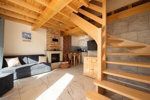 A living room with a sofa, fireplace, wooden staircase, and a kitchen area in the background. - Year-round holiday home with fireplace and terrace (Mielno)