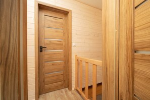Une porte en bois, dotée de traverses horizontales et d’une poignée en métal, qui donne sur une pièce avec une rambarde en bois et un plancher de couleur claire.