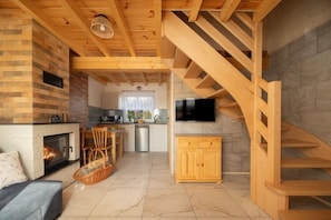 A spacious living area with a fireplace, wooden staircase, and a kitchen in the background. - Year-round holiday home with fireplace and terrace (Mielno)