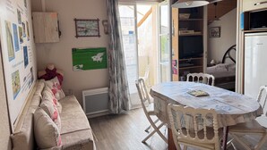Ein gemütliches Zimmer mit Holzbalkendecke, einem Esstisch mit Stühlen, einer Couch, einem Heizkörper und einem Fernseher.