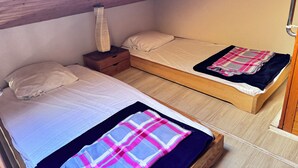 Ein kleines, gemütliches Zimmer mit zwei Einzelbetten, einem Nachttisch, einer Lampe und einer Holzbalkendecke.