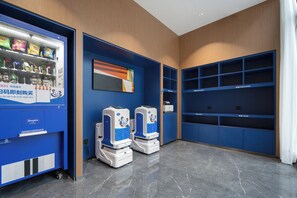 Un hall d’hôtel moderne équipé d’un distributeur automatique, de deux bornes de libre-service et de rangements bleus.