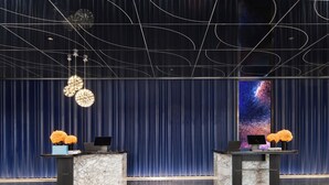 En hotellobby med marmorskivor i receptionsdisken, en stor digital skärm som visar en bild av en galax och en modern takdesign.