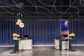 Zona de recepción de un hotel con mostradores de mármol, una gran pantalla digital mostrando una imagen de galaxia y un diseño de techo moderno.