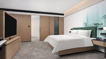 A modern hotel room with a large bed, a television, a desk with a phone, and a wardrobe.