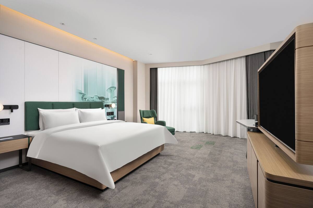 Ein modernes Hotelzimmer mit einem großen Bett, einem Flachbildfernseher, einem Schreibtisch und einem Sessel.