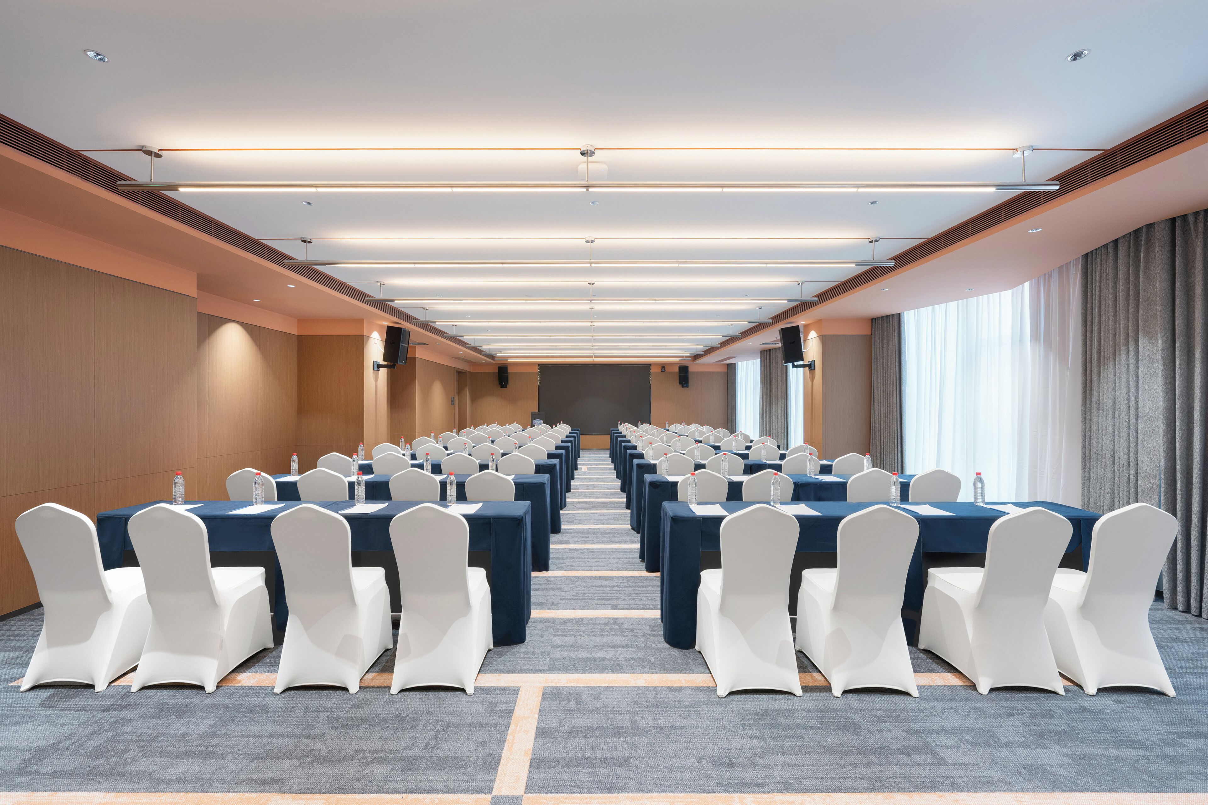 A conference room with rows of tables and chairs, a carpeted floor, and a long view towards the back.
