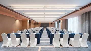 A conference room with rows of tables and chairs, a carpeted floor, and a long view towards the back.