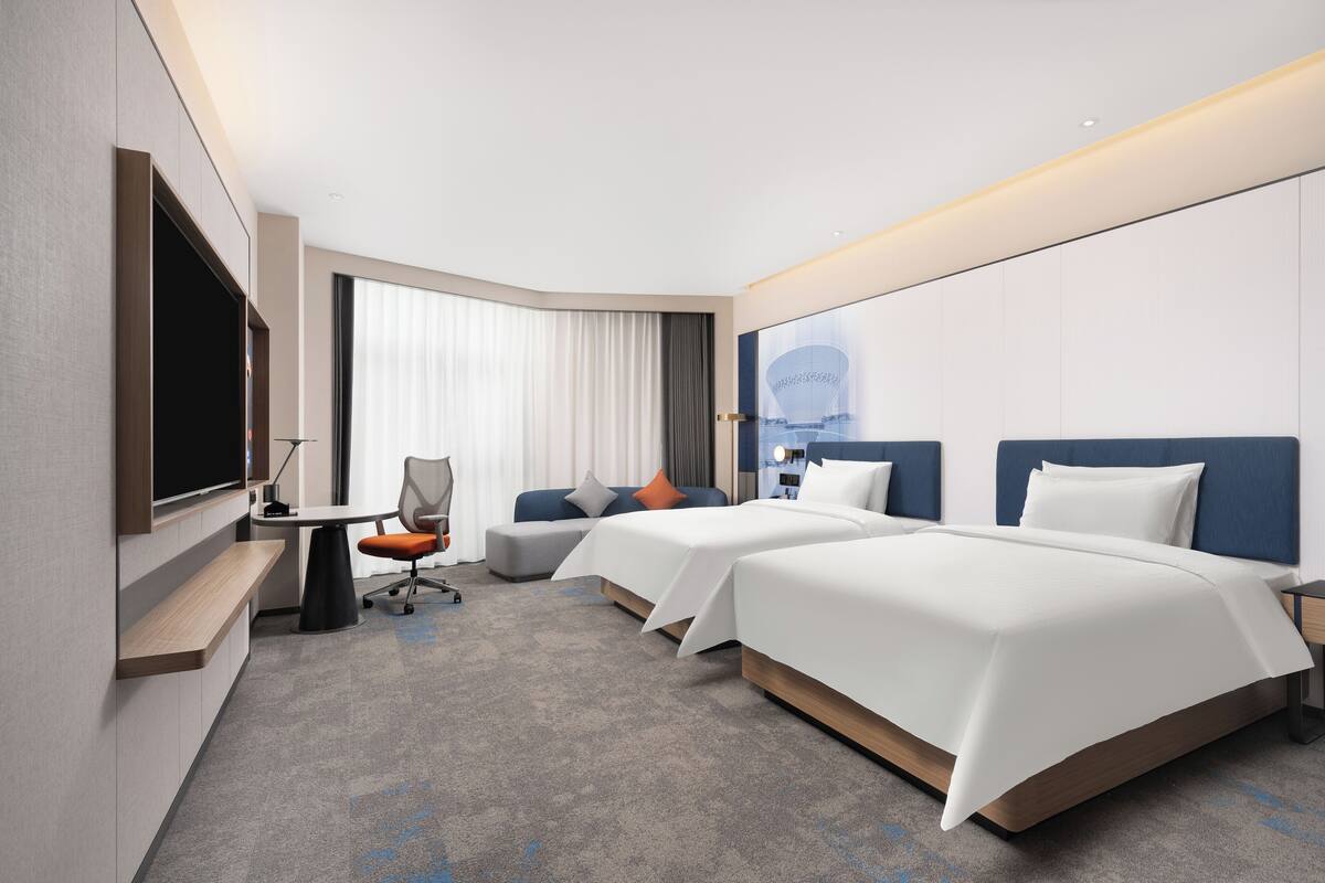 Ein Hotelzimmer mit zwei Betten, einem Schreibtisch, einem Sessel und einem Fernseher.