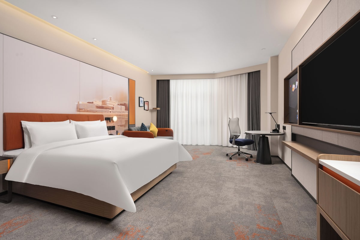 Ein Hotelzimmer mit Bett, Schreibtisch, Stuhl, Fernseher und Vorhängen.