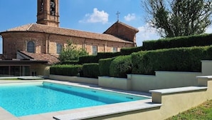Una piscina, un edificio con una torre y un seto cuidado.