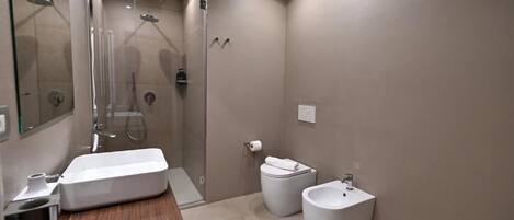 Une salle de bain moderne avec une douche à parois de verre, un meuble-lavabo en bois, un bidet et un petit lavabo.