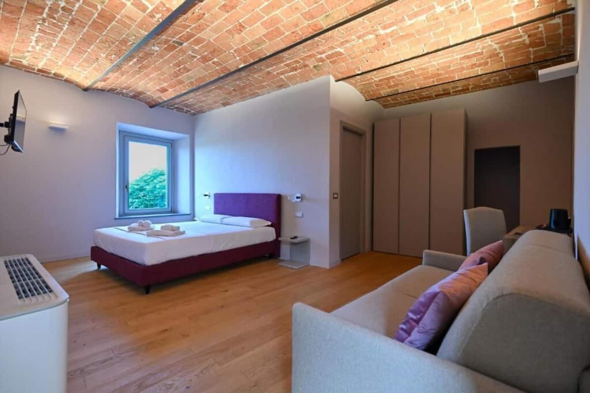 Un dormitorio moderno con techo de ladrillo, un ventanal grande, una cama, un armario y un sofá.