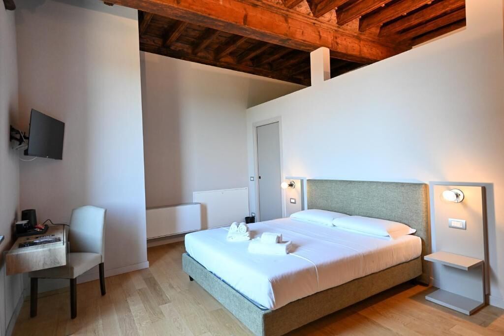 A bedroom with a bed, bedside tables, a chair, a desk, a television, and a wooden ceiling.