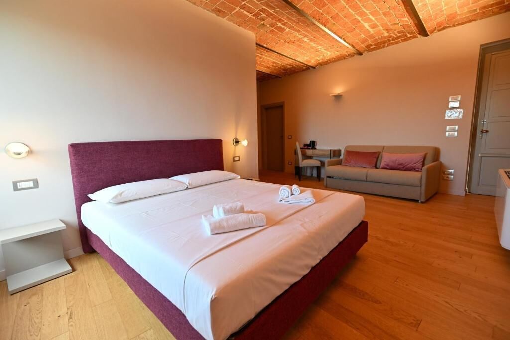 A hotel room with a large bed, a sofa, a desk, and a door.