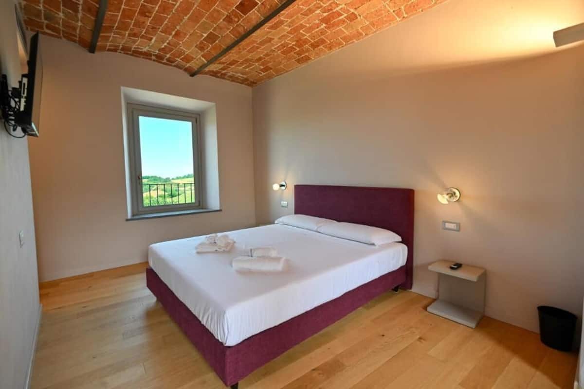 Un dormitorio con cama, ventana, mesita de noche y techo de ladrillo.