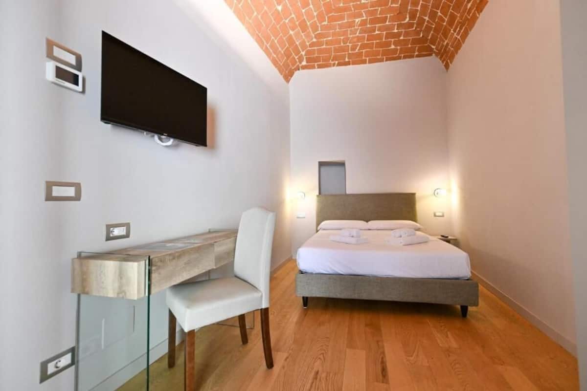 Un dormitorio con una cama, un escritorio y un televisor montado en la pared.