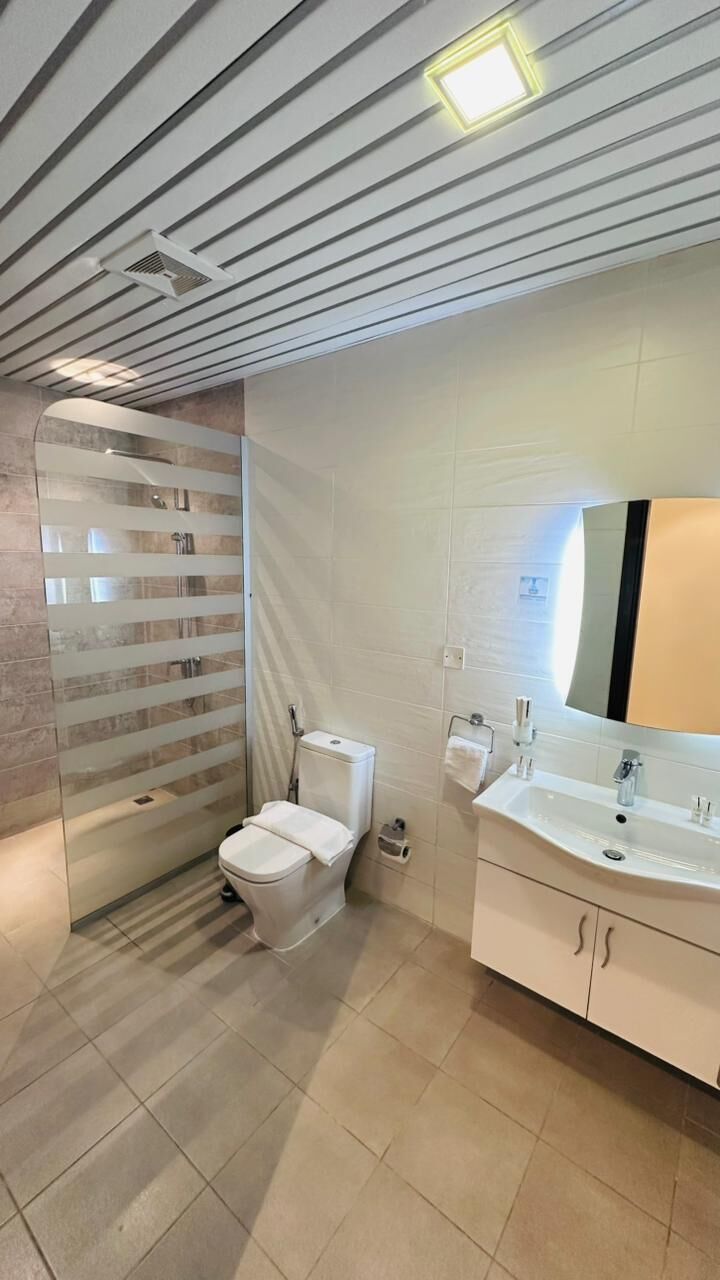 A modern bathroom with a glass shower enclosure, a toilet, a sink with a mirror, and a tiled floor.