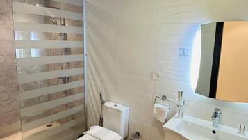 A modern bathroom with a glass shower enclosure, a toilet, a sink with a mirror, and a tiled floor.