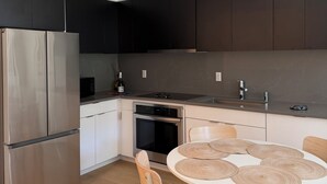 A modern kitchen with a stainless steel refrigerator, dark cabinets, a built-in oven, and a round dining table with wooden chairs. - 2 Beds Garden Condo in Fort Greene (Brooklyn)