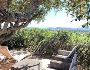 Terrassenmöbel aus Rattangeflecht, ein Holzzaun und Blick auf eine Landschaft mit Bäumen und Hügeln.