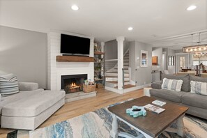 A modern living room with a fireplace, a flat-screen TV, a staircase, and a cozy seating area. - Walk to Beach & Restaurants | 4 Levels | Rooftop Deck | Remodeled & Updated Throughout (St. Simons Island)