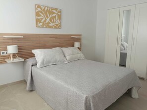 Ein Schlafzimmer mit Bett, Nachttischen, Kopfteil, Kleiderschrank und einem an der Wand hängenden Kunstwerk.