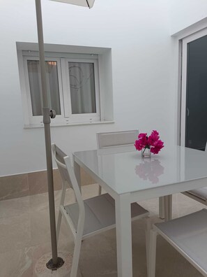 Ein weißer Tisch mit einer Vase voller rosa Blumen, ein Stuhl und ein Fenster mit Vorhängen.