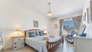Un dormitorio con cama, mesitas de noche, cómoda, espejo y ventana con cortinas.