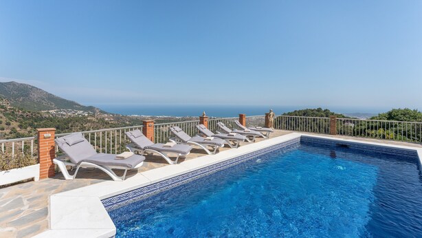 Una piscina con sillas de descanso, bordeado por baldosas y vista al mar.