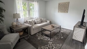 Een woonkamer met een bank, salontafel, bijzettafeltje, lamp en een televisie.