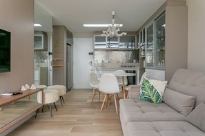 A modern kitchen with a dining area, a sofa, and a TV.