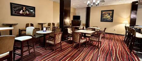 Un hall d’hôtel avec un tapis à rayures, plusieurs tables et chaises, un téléviseur et des œuvres d’art accrochées aux murs.