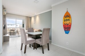 A dining area with a table and chairs, a surfboard decoration on the wall, and a view through a large window. - Wi-Fi 500MB | 150m from the beach | Pool #IA37 (Florianópolis)