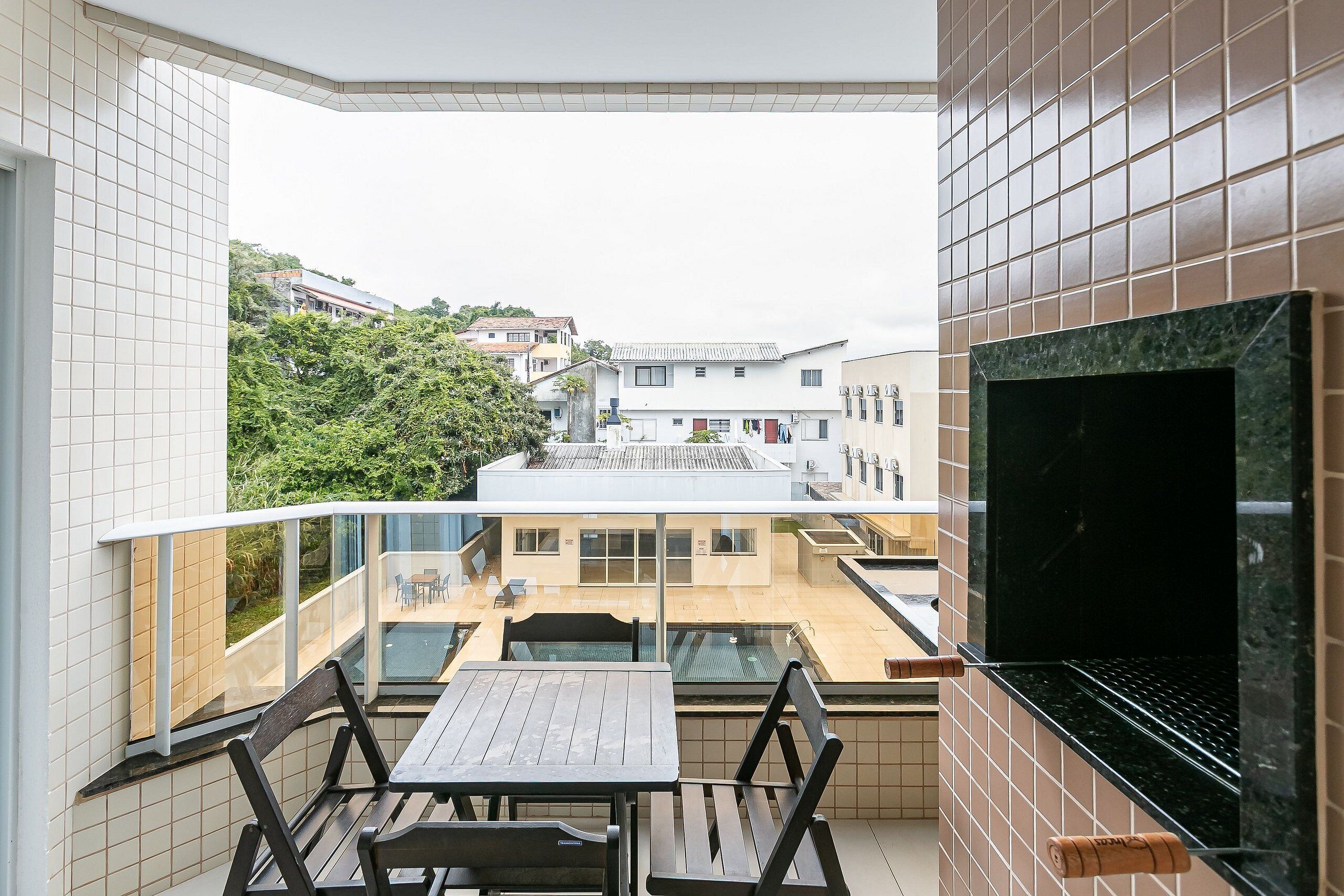 Un balcon avec une table et des chaises, un téléviseur et une vue sur les bâtiments et la verdure.