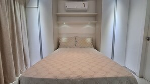 Ein schmaler Raum mit einem Bett, einer Decken-Klimaanlage und einer Tür an der Seite.