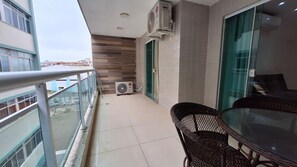 A balcony with a table and chairs, an air conditioning unit, and a glass door leading to a room. - O AP mais lindo da Praia do Forte 213 (Cabo Frio)