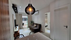 A modern living room with a sofa, a dining table, and a unique pendant light. - O AP mais lindo da Praia do Forte 213 (Cabo Frio)